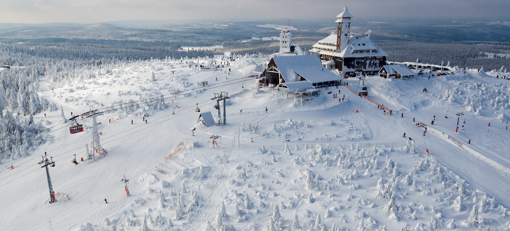 Ein Haus auf einem Berg, daneben Skipisten auf denen Skifahrer fahren.