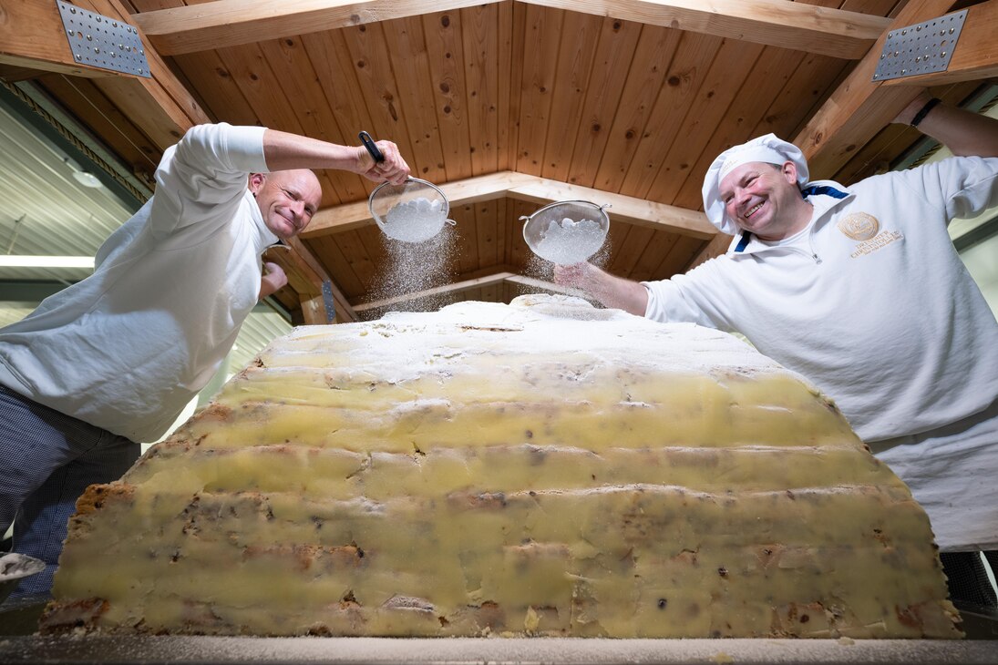 Zwei Bäcker bestreuen einen Riesenstollen mit Puderzucker.